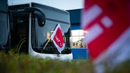 Eine verdi-Fahne hängt an einem geparkten Linienbus auf dem Betriebshof der Autokraft GmbH. © picture alliance/dpa Foto: Jonas Walzberg