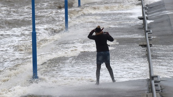 ARCHIV - Wellen überspülen am 09.01.2015 den Fähranleger in Dagebüll (Schleswig-Holstein), während eine Frau gegen den Wind kämpft. © picture alliance / Carsten Rehder/dpa Foto: Carsten Rehder