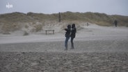 Menschen lehnen sich auf einem Sandstrand in den dort wehenden Wind © NDR Foto: NDR Screenshot