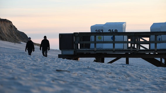 Kampen: Zwei Menschen gehen bei Sonnenuntergang am Strand von Kampen. © dpa Foto: Lea Albert