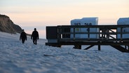 Kampen: Zwei Menschen gehen bei Sonnenuntergang am Strand von Kampen. © dpa Foto: Lea Albert