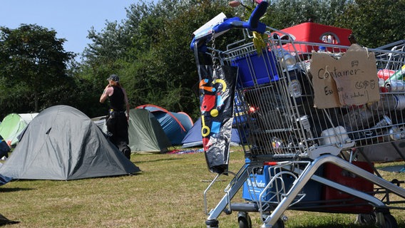 Ein Teilnehmer des Punk-Protestcamps geht hinter einem Einkaufswagen und zwischen Zelten über die Camp-Wiese © dpa-Bildfunk Foto: Lea Albert