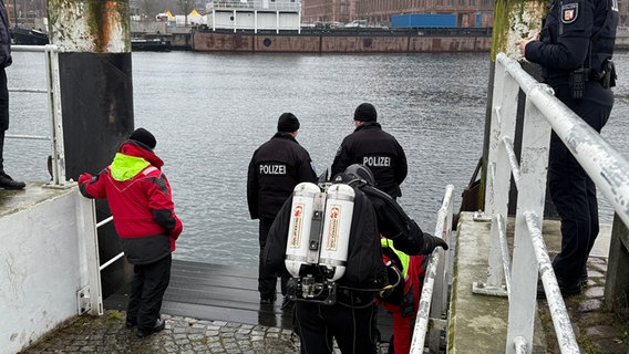 Zwei Polizeibeamte stehen nah am Hörnbecken in Kiel, hinter ihnen ein Taucher, der sich fertigmacht. © NDR Foto: Tobias Gellert