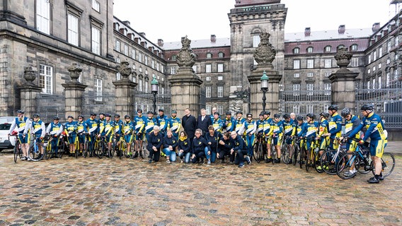 Ein großes Team von Radfahrern steht in einem Halbkreis vor einem historischen Gebäudekomplex in Kopenhagen. © Der Nordschleswiger - Walter Turnowski Foto: Walter Turnowski