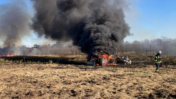 Ein brennender Traktor steht auf einem Feld, während die Feuerwehr mit den Löscharbeiten beginnt. © NDR Foto: Carsten Rauterberg