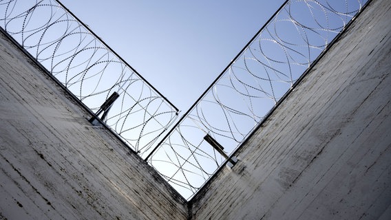 Stacheldraht säumt die Mauern in einem Gefängnis, der Blick geht an den Mauern entlang in den Himmel. © picture alliance/KEYSTONE | ENNIO LEANZA Foto: ENNIO LEANZA