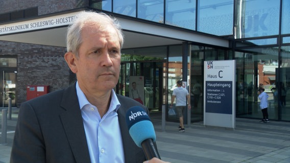Ein Mann gibt ein Interview vor dem Eingang des UKSH in Kiel, es ist Jens Scholz, der Vorstandsvorsitzende des Universitätsklinikums Schleswig-Holstein © NDR Foto: NDR Screenshot