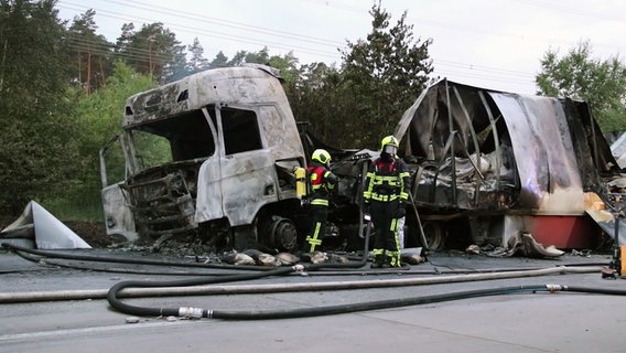 Zwei Feuerwehrleute stehen an einem ausgebrannten Lkw nach einem Unfall auf der A24. © DSLRNews 