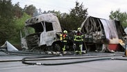 Zwei Feuerwehrleute stehen an einem ausgebrannten Lkw nach einem Unfall auf der A24. © DSLRNews 