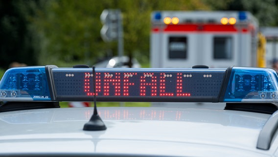 Streifenwagen der Polizei mit Blaulicht und dem Schriftzug Unfall im Display an einem Unfallort. Im Hintergrund sieht man einen Rettungswagen © Picture Alliance Foto: Fotostand/Gelhot