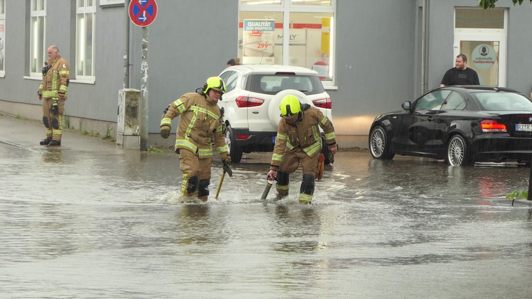 Während eines Unwetters laufen Feuerwehrleute über die Straße durch Knietiefes Wasser