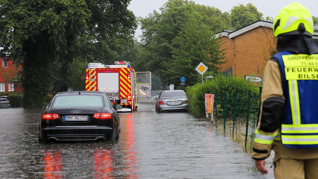 Ein Auto fährt hinter einem Feuerwehrwagen durch eine überflutete Straße.