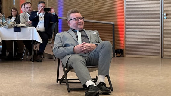 Eine Person sitzt in einem Konferenzsaal in einem Liegestuhl, es ist Hans-Jürgen Lütje, der ehemalige Bürgermeister von Büsum. © NDR Foto: Kristina Heinicke