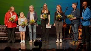 Auf einer Bühne stehen mehrere Personen in einer Reihe © NDR Foto: NDR Screenshot