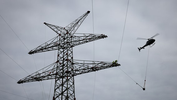 Ein Hubschrauber fliegt beim Einziehen der sogenannten Vorseile zwischen Strommasten der Ostküstenleitung. © picture alliance/dpa Foto: Christian Charisius