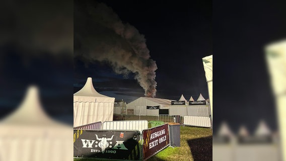 Hinter einem Zelt beim Wacken-Festival ist eine Rauchsäule zu sehen, die in den Nachthimmel steigt. © NDR Foto: Frank Figge