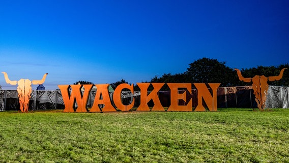 Wacken: Das Festival-Logo gefertigt aus großen Metallbuchstaben, steht auf einer Wiese. © dpa Foto: Axel Heimken