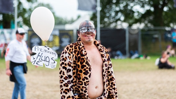 Ein Mann, nur mit Hose und Leoparden-Bademantel bekleidet, zieht ein Pappschild, das von einem Luftballon getragen wird. © NDR Foto: Dominik Dührsen