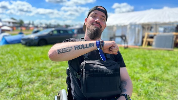 Ein rollstuhlfahrener Mann präsentiert ein Tattoo auf seinem Unterarm, das Tattoo ist der Text: "Keep Rolling" © NDR Foto: Jörn Zahlmann