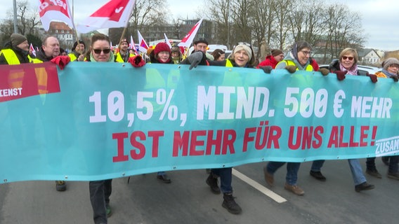 Demonstrierende tragen ein Banner vor sich mit der Aufschrift: " 10,5 Prozent, mind. 500 Euro mehr" © NDR 