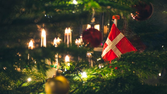 Ein Weihnachtsbaum von nahmen, mit Kerzen, Kugeln und einer Dänemarkflagge geschmückt. © IMAGO / Depositphotos 