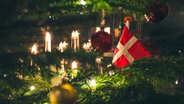 Ein Weihnachtsbaum von nahmen, mit Kerzen, Kugeln und einer Dänemarkflagge geschmückt. © IMAGO / Depositphotos 