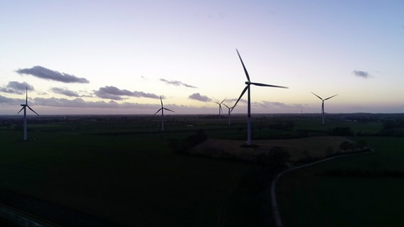 Mehrere Windkraftanlagen stehen im Windpark Neuengörs bei Dämmerung. © NDR 