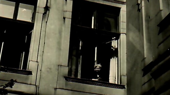 Eine Schwarzweißaufnahme zeigt wie ein Kind aus einem Fenster blickt © NDR Foto: NDR Screenshot