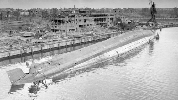 Eine Schwarzweißaufnahme eines gekenterten Schiffes in einem Hafen © NDR Foto: NDR Screenshot