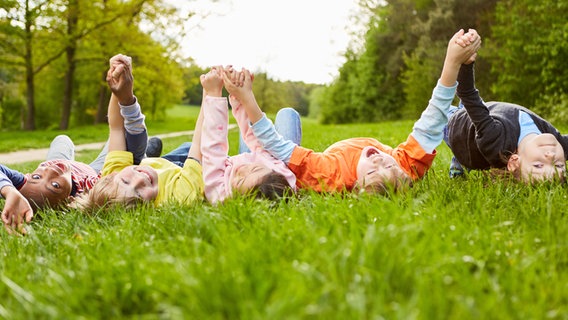 Kinder liegen auf einer Wiese und halten sich an den Händen © picture alliance / Zoonar | Robert Kneschke Foto: Robert Kneschke