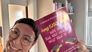 Martina Gilica hält das Buch "Jung (Ü50) sucht - Habe Falten, sehe aber auch deine nicht mehr so gut" in der Hand. © NDR 