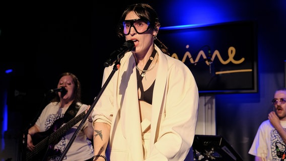 Mine auf der Bühne bei ihrem Auftritt in der Reihe stars@ndr2 am 23. Mai 2024 in Hamburg - mit großer Brille und beigem Jacket © NDR 2 Foto: Viktoria Wanka