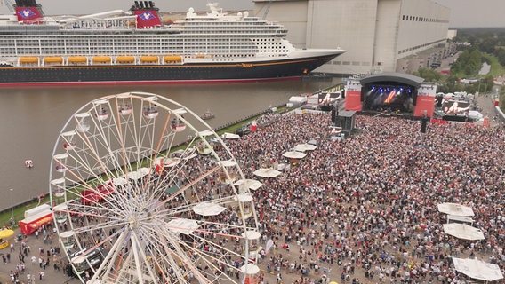 Bllick aus der Luft auf das Festivalgelände mit der Bühne, den Videowänden und dem Kreuzfahrtschiff "Disney Treasure" im Hintergrund © NDR 2 Foto: Axel Herzig