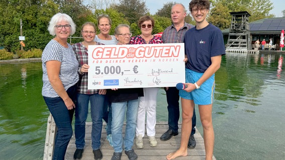 NDR 2 Reporter Jelto (re.) überreicht den Scheck über 5.000 Euro auf einem Steg im Freibad Gronau/L. © NDR 2 