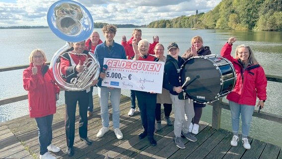 Die Gewinner von "Geld für die Guten" am 2. Oktober, der Musikzug Plön, steht mit NDR 2 Reporter Jelto auf einem Steg am Plöner See © NDR 2 Foto: Olli Schönhoff