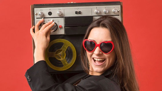 Frau mit langen Haaren und Herrzchen-Brille hat ein Tonband-Gerät am Ohr © IMAGO / imagebroker 