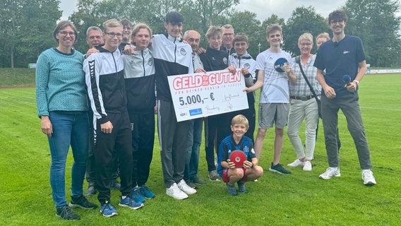 Scheckübergabe: NDR 2 Reporter Jelto Ringena (re.) mit mehreren jungen Sportlern auf einem Fußballplatz © NDR 2 Foto: Moritz Kleßmann