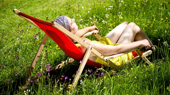 Junge Frau liegt entspannt auf einer Blumenwiese in einem Liegestuhl © Fotolia.com Foto: Almgren