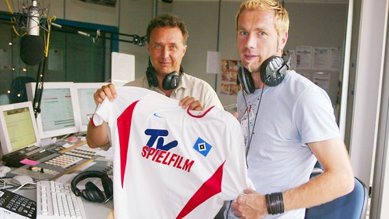 Uwe Bahn steht neben HSV-Stürmer Sergej Barbarez im Studio, beiden halten ein HSV-Trikot hoch (2002) © NDR 