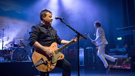 Die walisische Rockband Manic Street Preachers bei einem Konzert in London. Im Vordergrund singt James Dean Bradfield und spielt Gitarre. © IMAGO / Matrix 