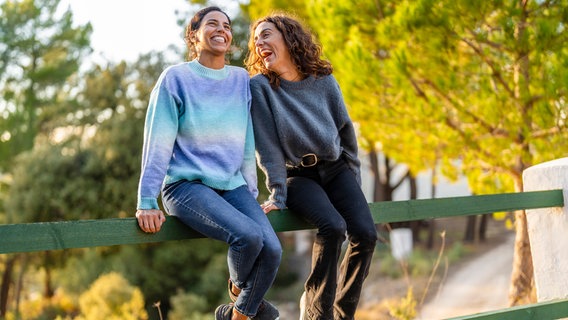 Cheerful friends sitting on railing at park © picture alliance / Westend61 | Javier De La Torre 