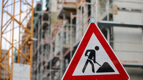 Ein Baustellenschild steht vor der Baustelle mehrerer Miethäuser. © picture alliance/dpa | Jan Woitas 