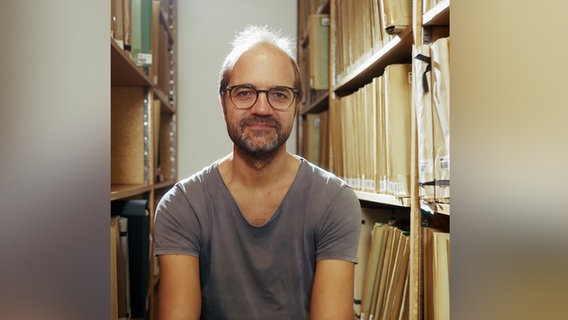 Jan Larsen, Solo-Bratschist des NDR Elbphilharmonie Orchesters, sitzt zwischen Regalen des NDR Notenarchivs. © NDR 