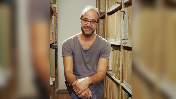 Jan Larsen, Solo-Bratschist des NDR Elbphilharmonie Orchesters, sitzt zwischen Regalen des NDR Notenarchivs. © NDR Foto: Screenshot