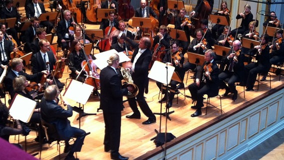 Konzertszene: Thomas Hengelbrock dirigiert das NDR Sinfonieorchester, Solist Jens Plücker steht mit seinem Horn vor dem Orchester. © NDR Sinfonieorchester 