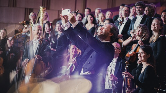 Stanislav Kochanovsky macht ein Selfie mit den Musiker:innen der NDR Radiophilharmonie beim Fotoshooting mit Nikolaj Lund © NDR Foto: Peer Bothmer