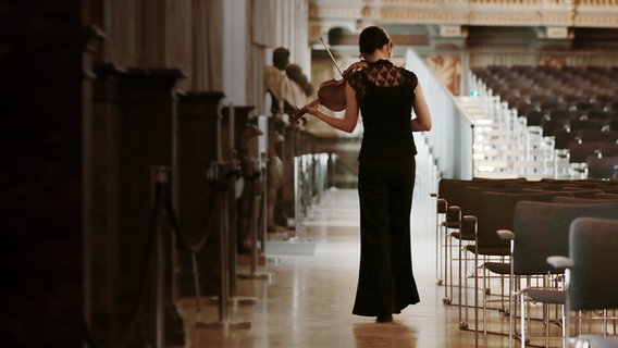 Eine Streicherin läuft mit ihrem Instrument durch den Saal im Schloss Herrenhausen und spielt dabei. © NDR Foto: Micha Neugebauer