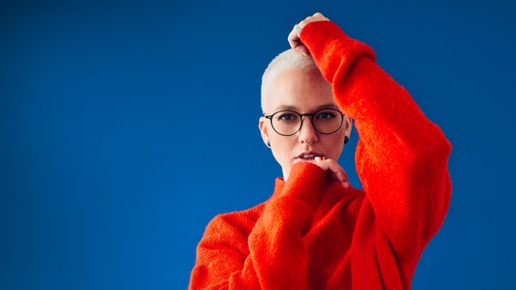 Eine Frau im roten Pullover vor blauem Hintergrund. © Maximilian König Foto: Maximilian König