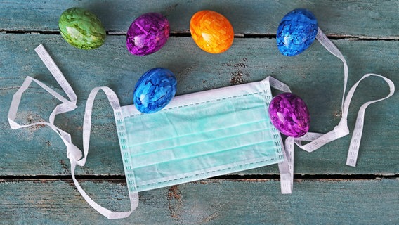 Easter eggs lie next to a face mask on a wooden background.  © COLOURBOX Photo: Astrid Gast