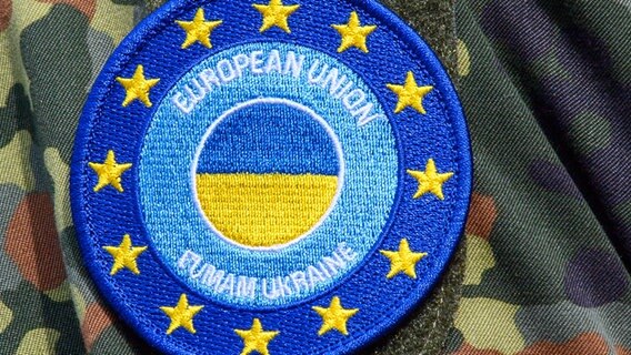 Die Deutsche Fahne und das Wappen der "European Union Military Assistance Mission in support of Ukraine" ist auf dem Truppenübungsplatz auf der Schulter eines Soldaten zu sehen. © picture alliance/dpa | Klaus-Dietmar Gabbert 